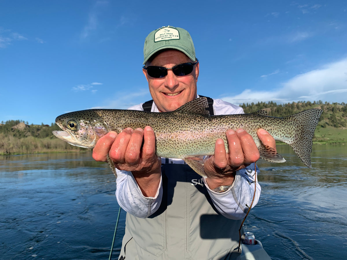 Angler holding a large Missouri River rainbow trout under a blue sky